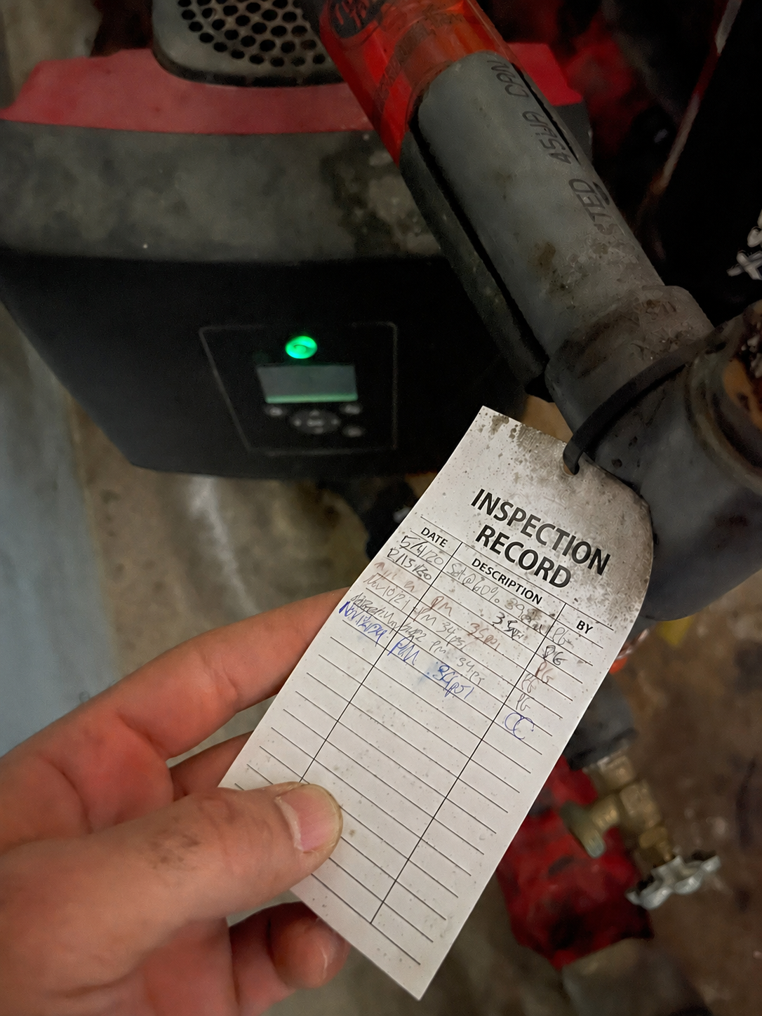 Handwritten inspection record held in front of a circulation pump — the paper tag MechaFlow replaces